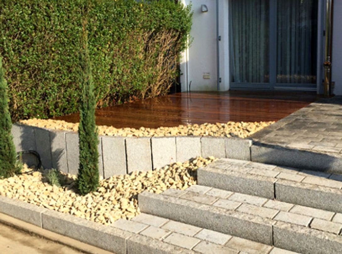 Granitstufen fuehren von einer Terrasse in den Garten, seitlich ein Kiesbett mit Saeulenzypressen vor einer dicht bewachsenen Efeuwand.